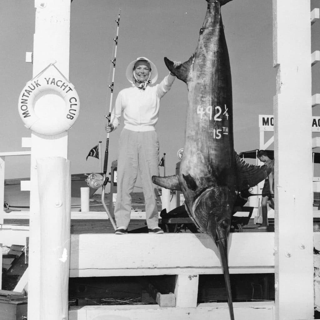 Black and white image of a woman standing next to a broadbill swordfish.