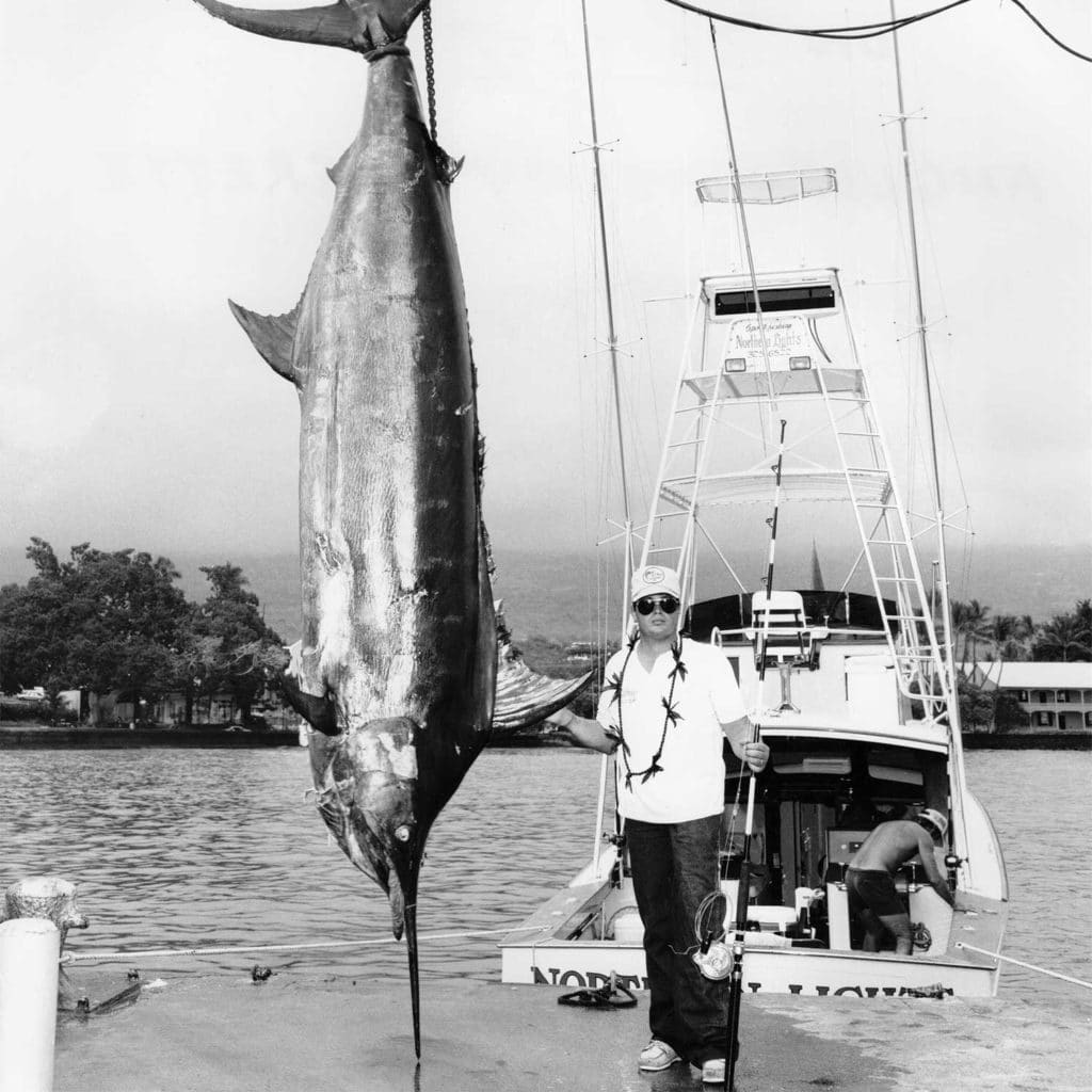 Black and white image of Kelley Everette next to a grander Kona blue marlin.