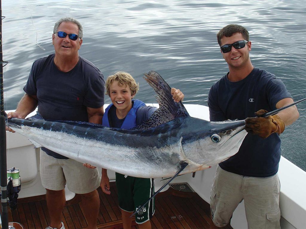 Two men and a young boy hold up a white marlin