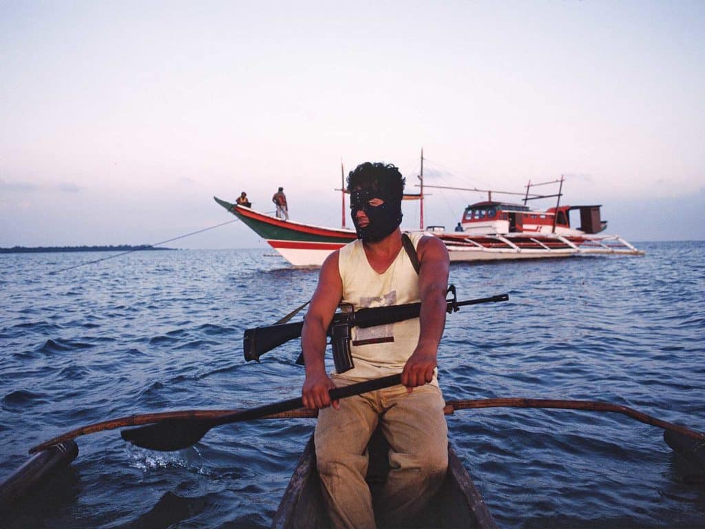 A pirate wearing a balaclava mask while rowing a dinghy.