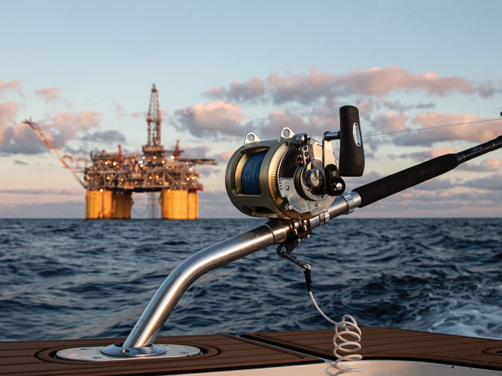 A close up image of a fishing reel with an oil right on the ocean in the distance.