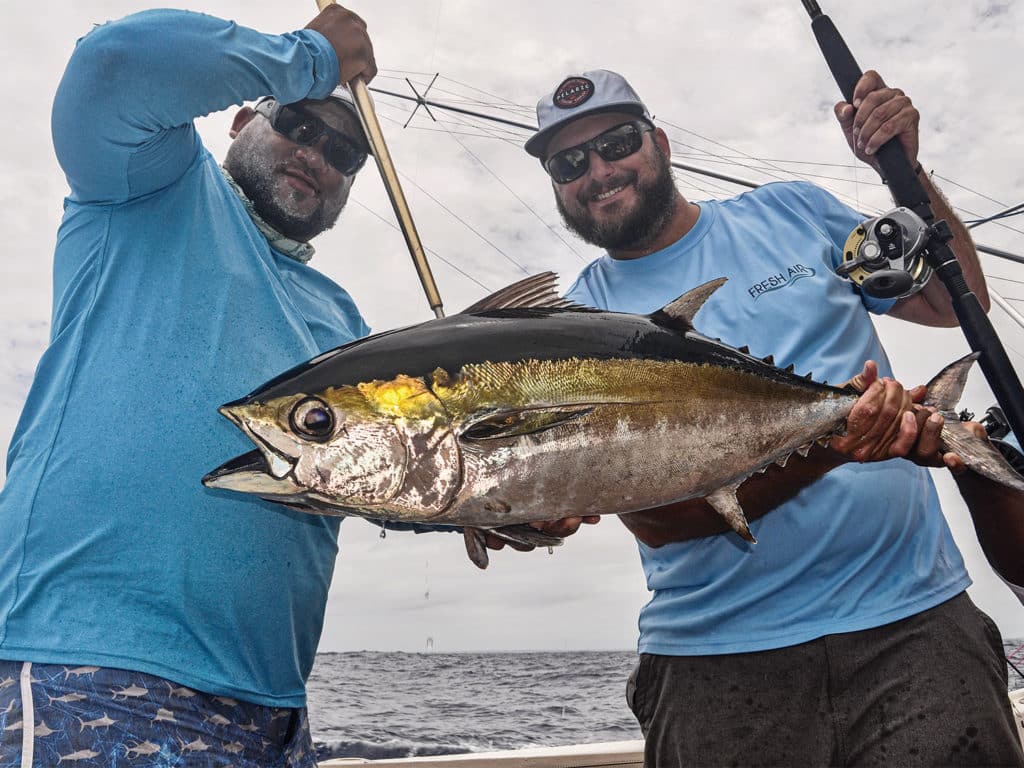 Two sport-fishing anglers hold up a large blackfin tuna.