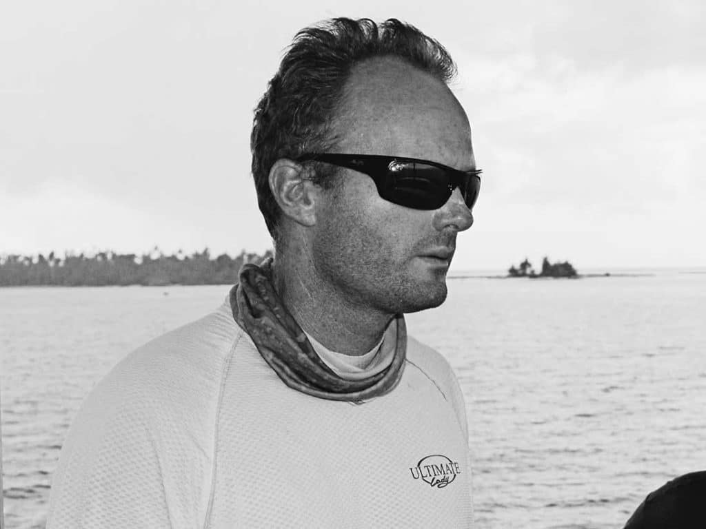 Black and white image of Capt. Tom Francis at the helm wearing sunglasses.