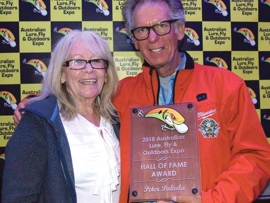 A man and his wife stand smiling while he holds an award.