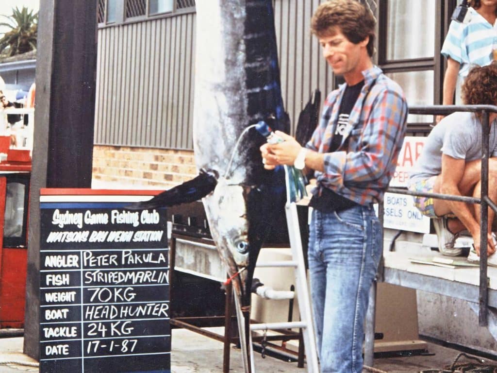 A man stands in front of a sign, and a large marlin.