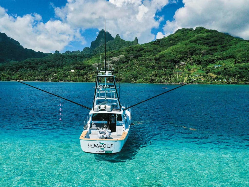 A sport-fishing boat rests in the waters of Tahiti, with island mountains on the horizon.