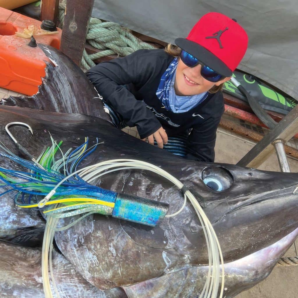 A young kid posing next to a large blue marlin.