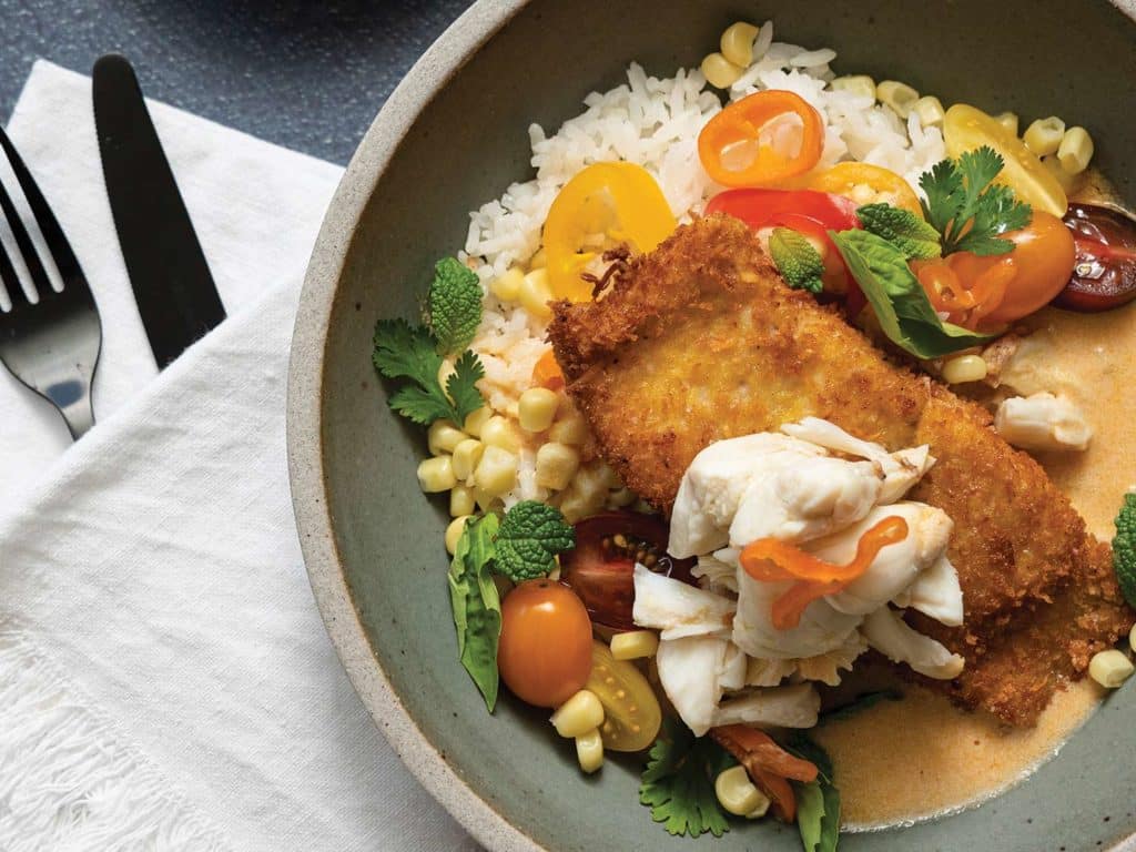 A plate of fried snapper, topped with crab and coconut-basil cream sauce over a bed of jasmine rice.