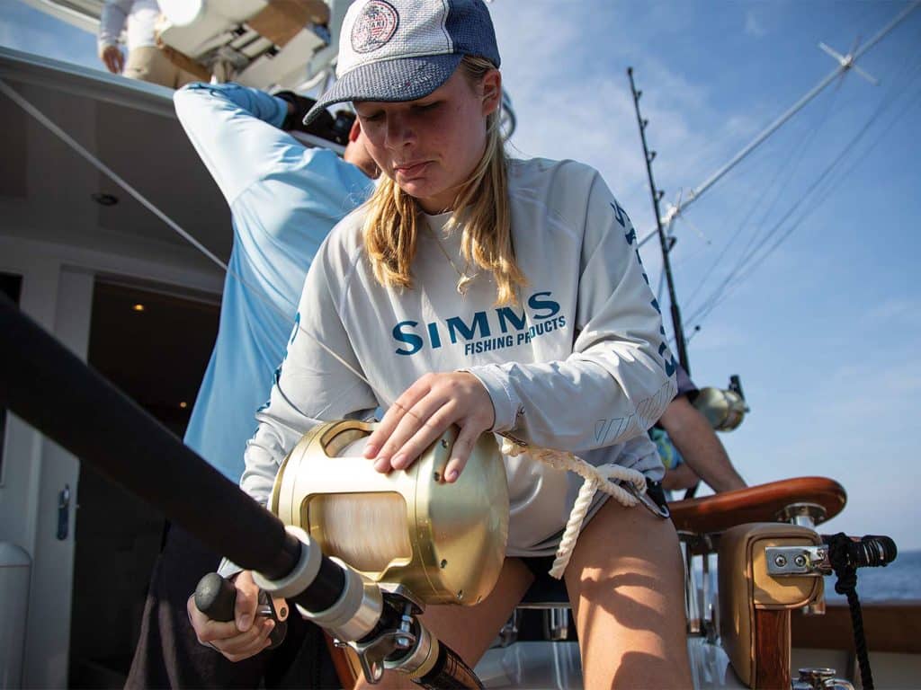 A young woman looms over a heavy-tackle saltwater fishing rod, in preparation for fishing.