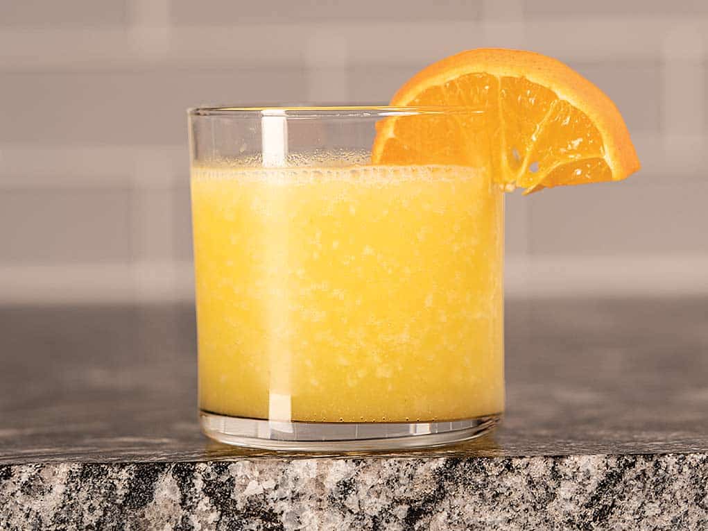 A small cocktail glass filled with orange and Tito's Homemade Vodka, garnished with an orange slice.