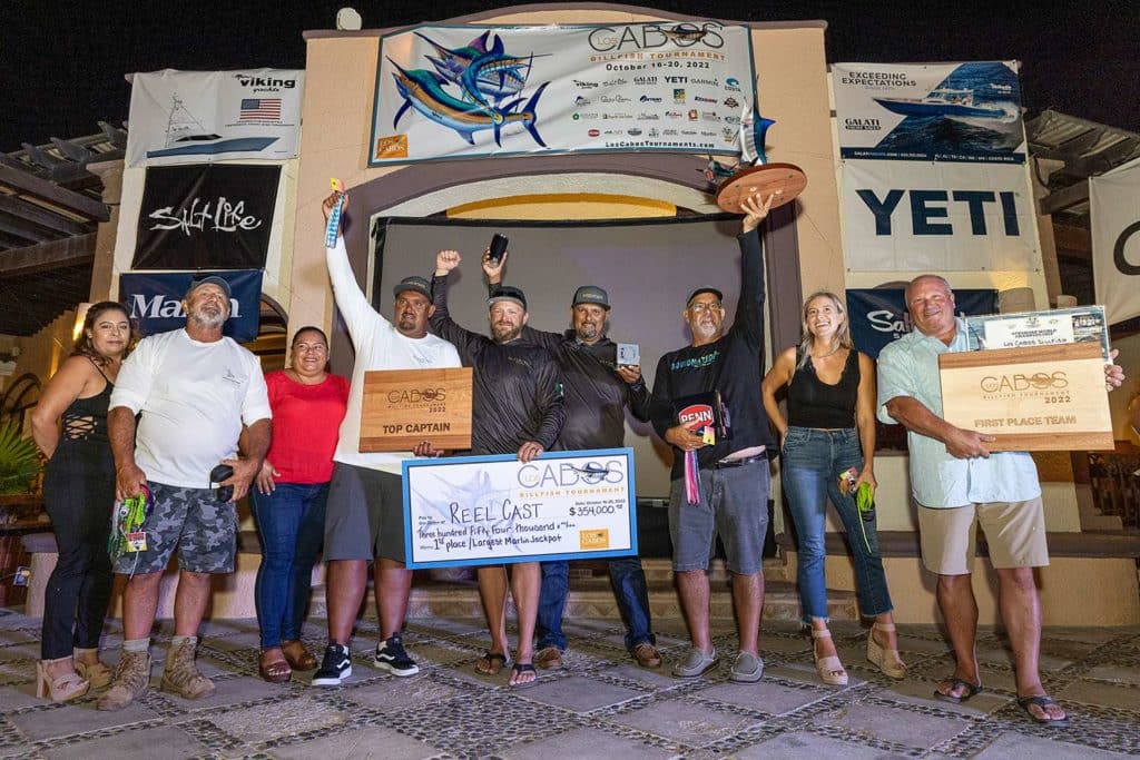 A sport-fishing team stands at an awards ceremony, holding trophies and a large check.