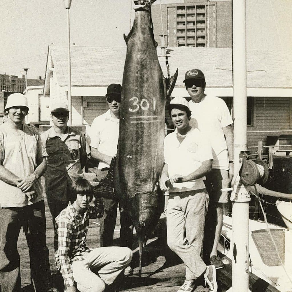 A black and white image of a group of anglers standing next to a large marlin.