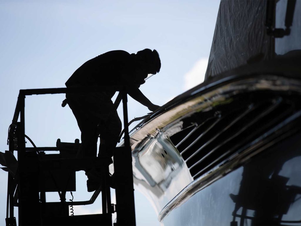 A silhouette of a custom boat builder working on a boat hull.