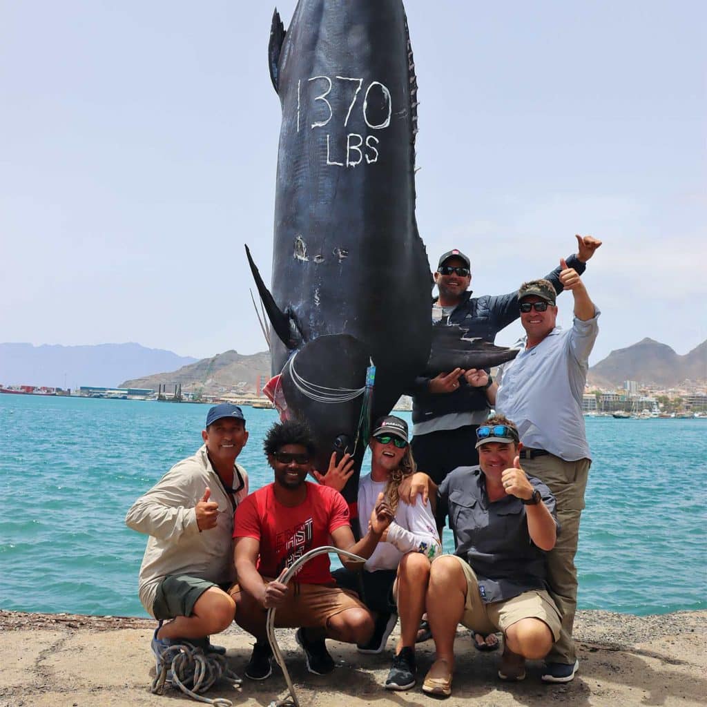 A sport-fishing team posing next to a large marlin.