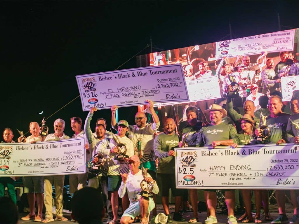 Several sport-fishing teams celebrating at an awards ceremony while holding up over-sized checks.