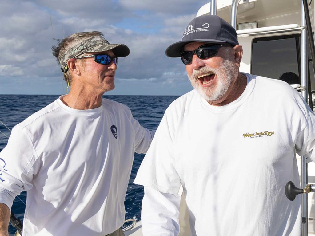 Two anglers smiling happily on a boat deck while fishing.