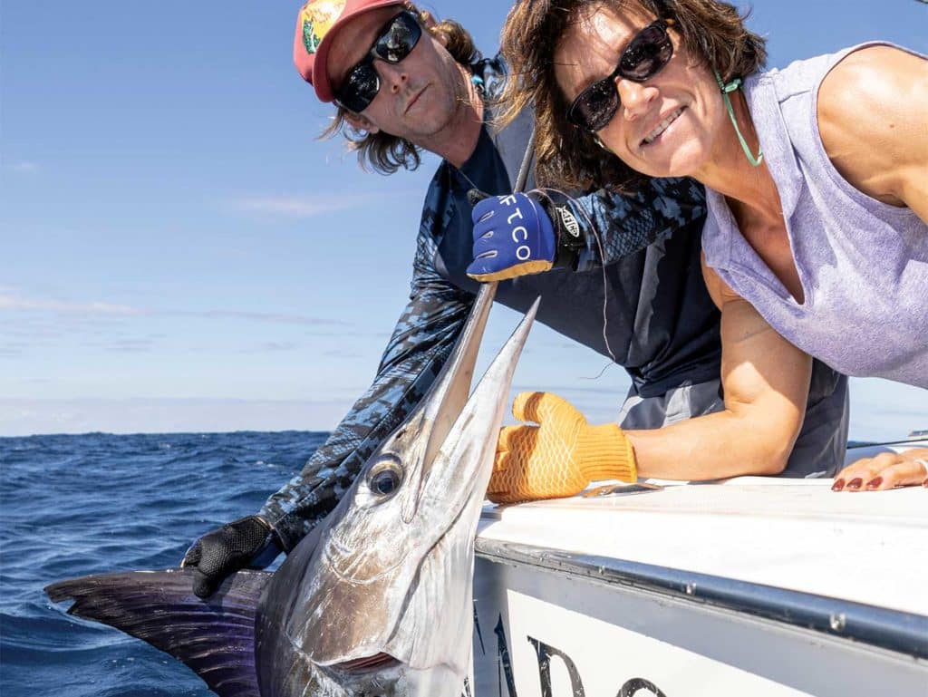 A woman holding a striped marlin by the bill, holding it boatside.