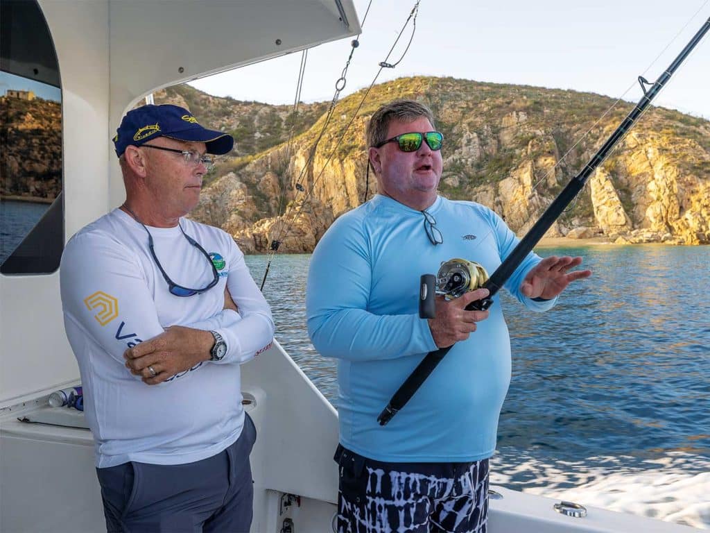 Two anglers on a boat, one is holdinng a fishing reel.