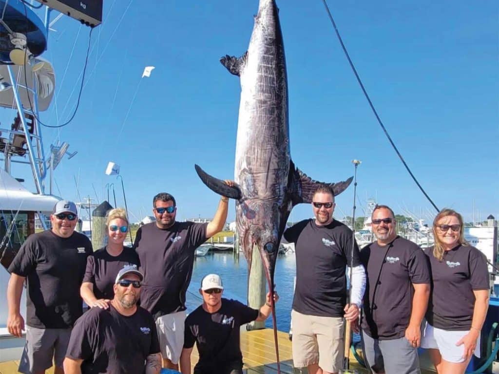 A fishing crew posing beside a large swordfish