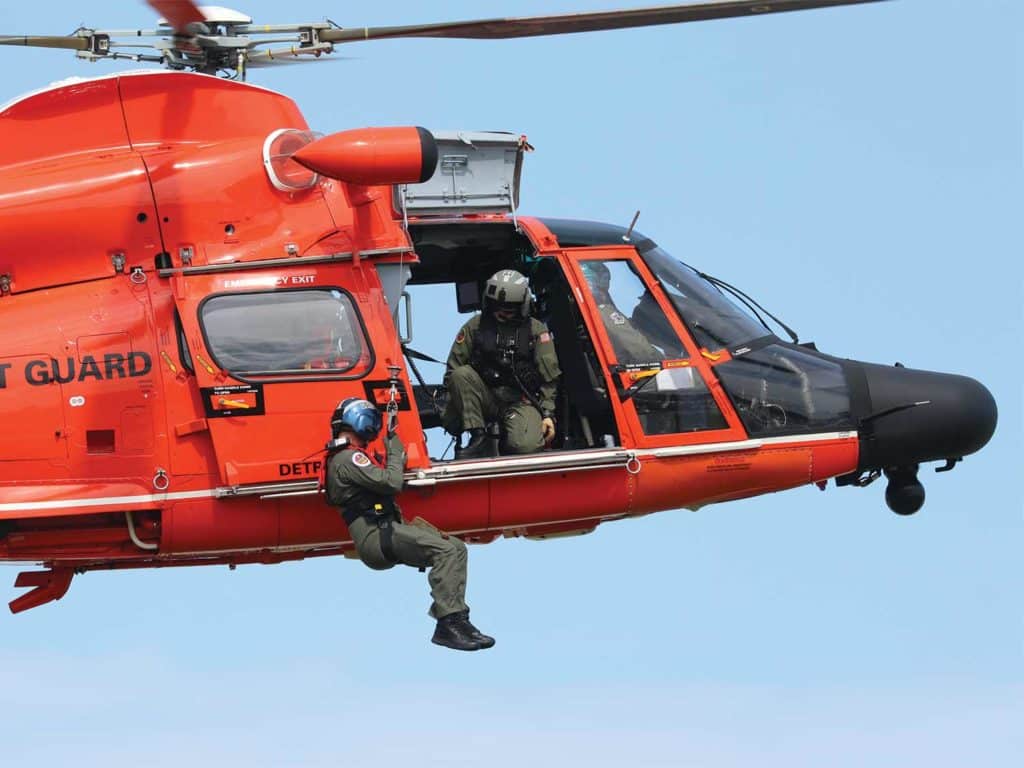 An orange US Coast Guard helicopter being piloted through the air.