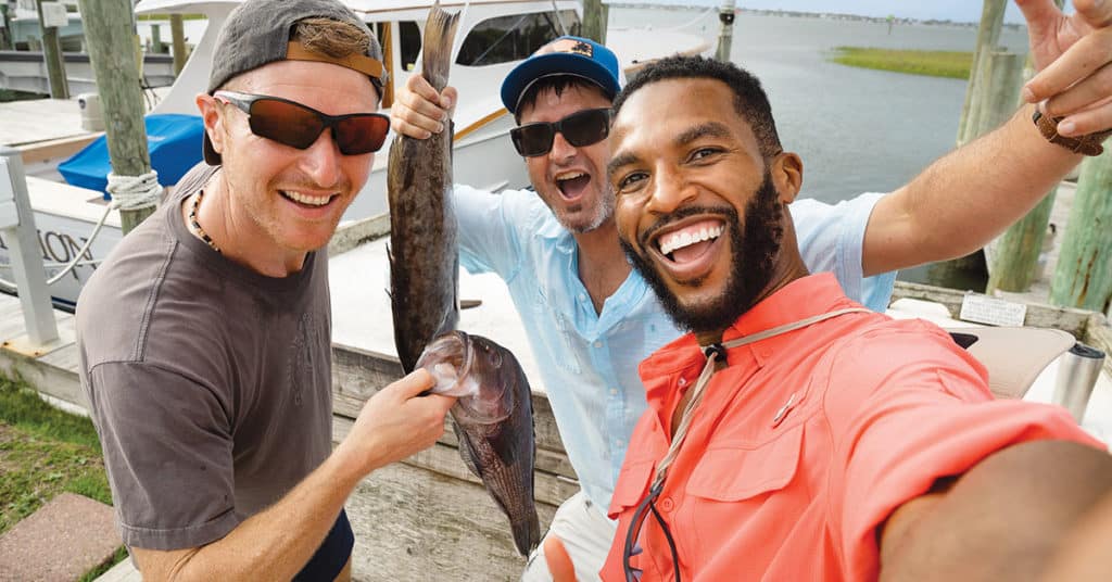 Three anglers smiling and holding up fish.
