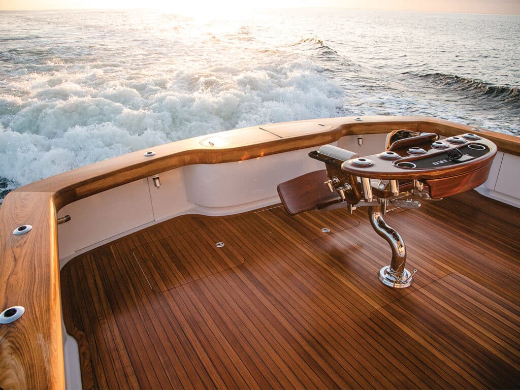 The cockpit of a custom Bayliss Boatworks sport-fishing boat, showing a fighting chair and the cresting waves from the boat in the ocean.