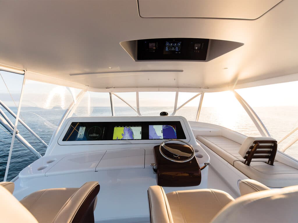 The helm of the custom Bayliss Boatworks sport-fishing boat shows a full-view of the sun setting over the ocean.