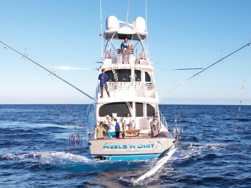 A sport-fishing boat cruising across water while an angler pulls in a large marlin.