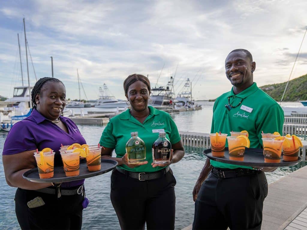 Three workers holding up trays of cocktails in a marina.