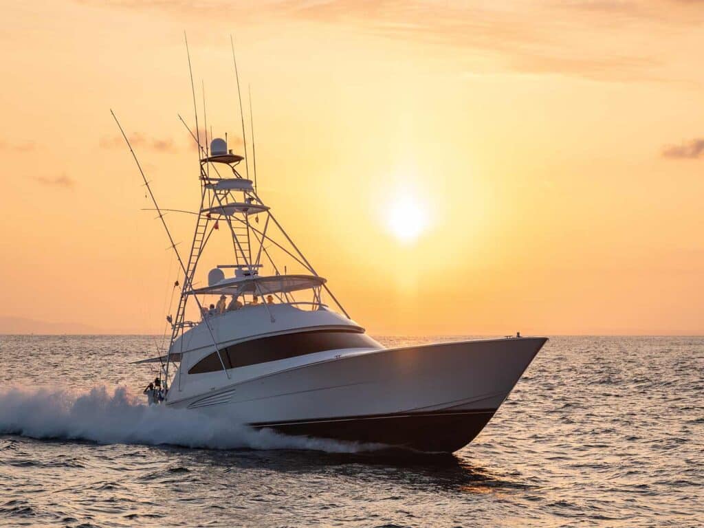 A sport-fishing boat cruises across the water at sunset, the sun hanging low in the horizon.