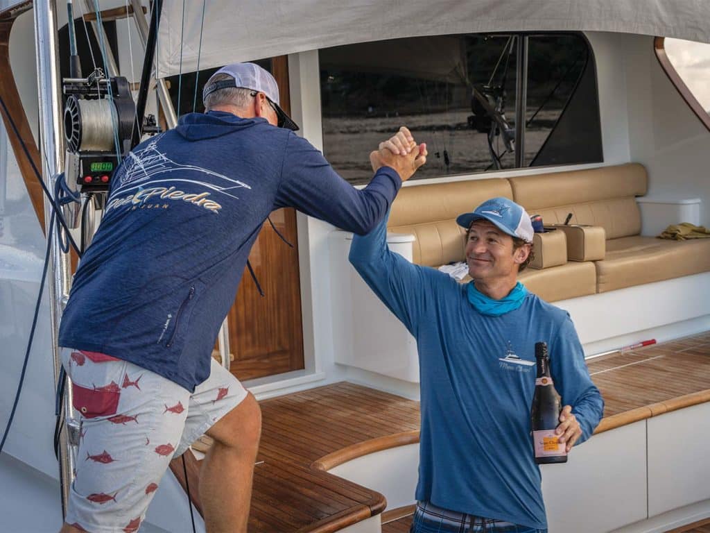 Two anglers high-fiving in the cockpit of a sport-fishing boat.