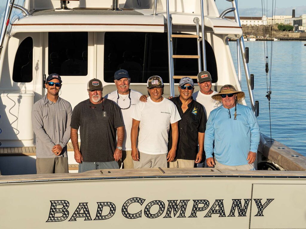 A team stands on the deck of a sport-fishing boat called Bad Company.