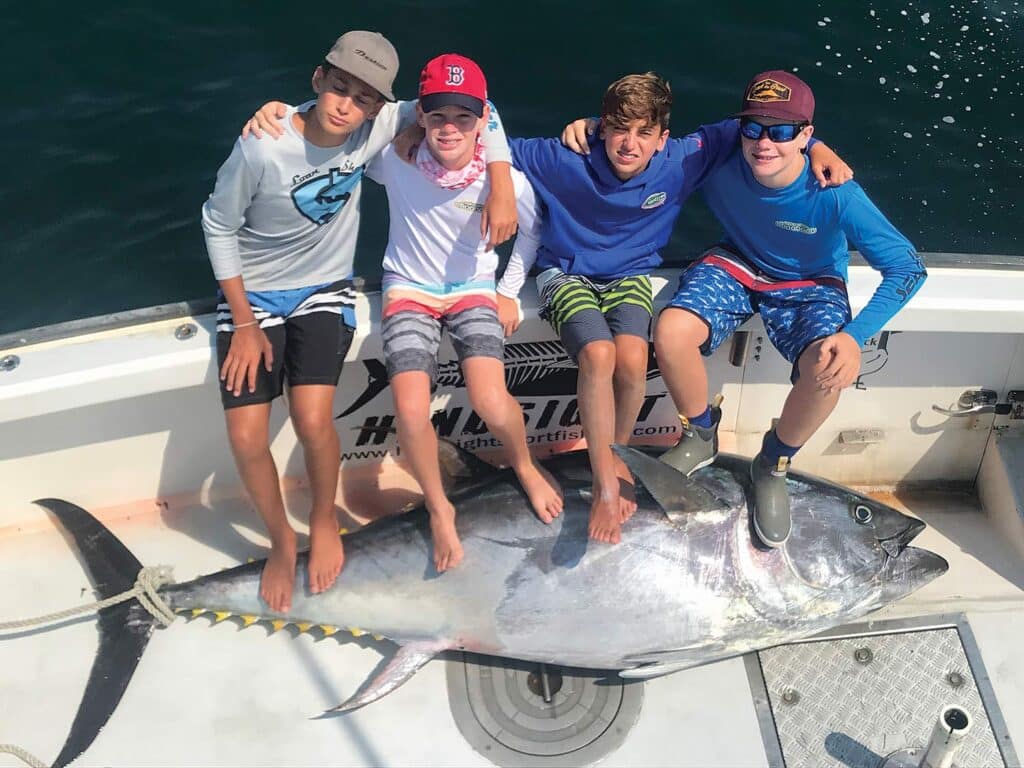 Four young boys sitting in the cockpit of a sport-fishing boat next to a large bluefin tuna.