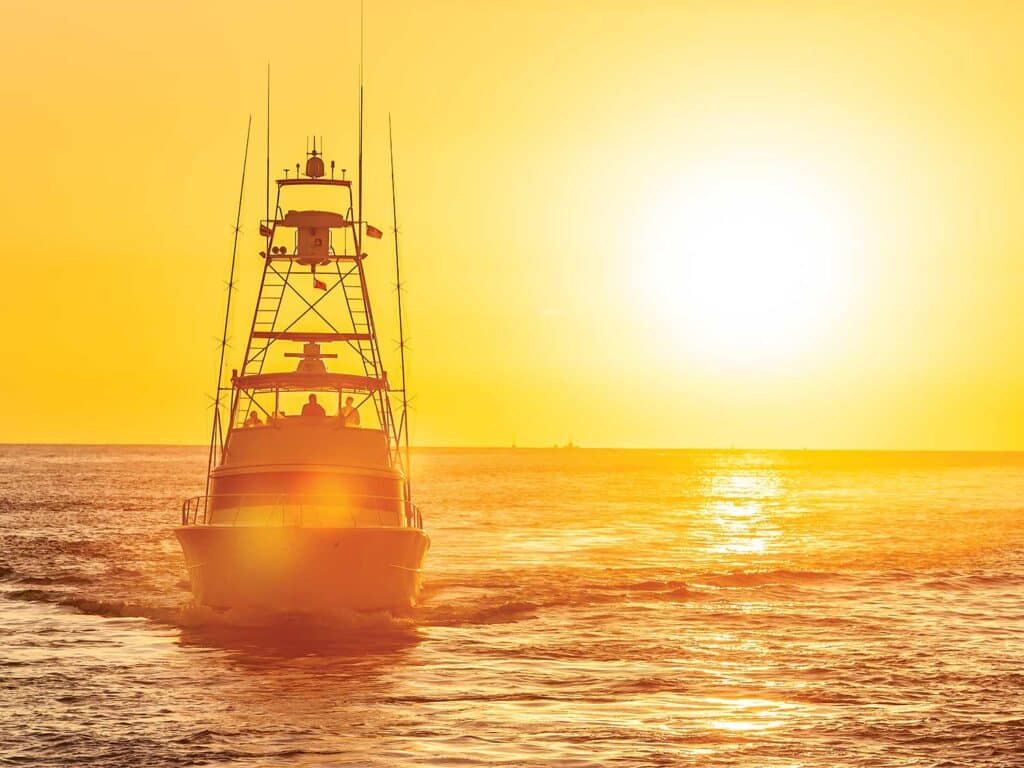A sport-fishing boat cruises across the water as the hot sun sets on the horizon.