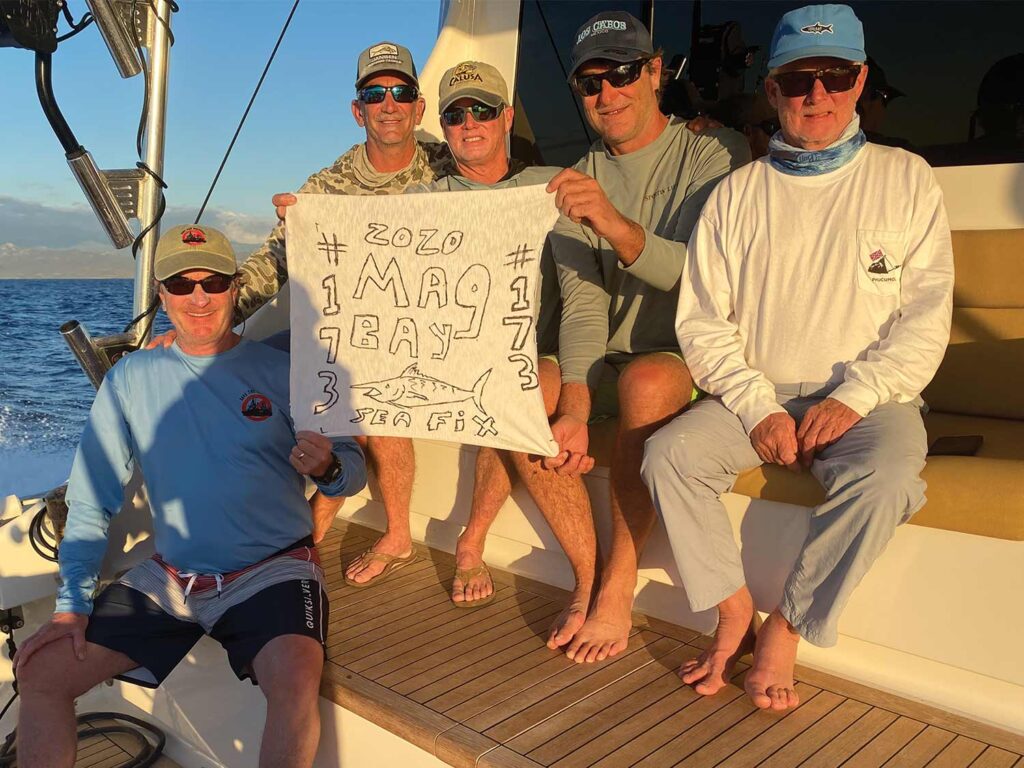 A group of anglers sitting in the cockpit of a sport-fishing boat holding up a sign.
