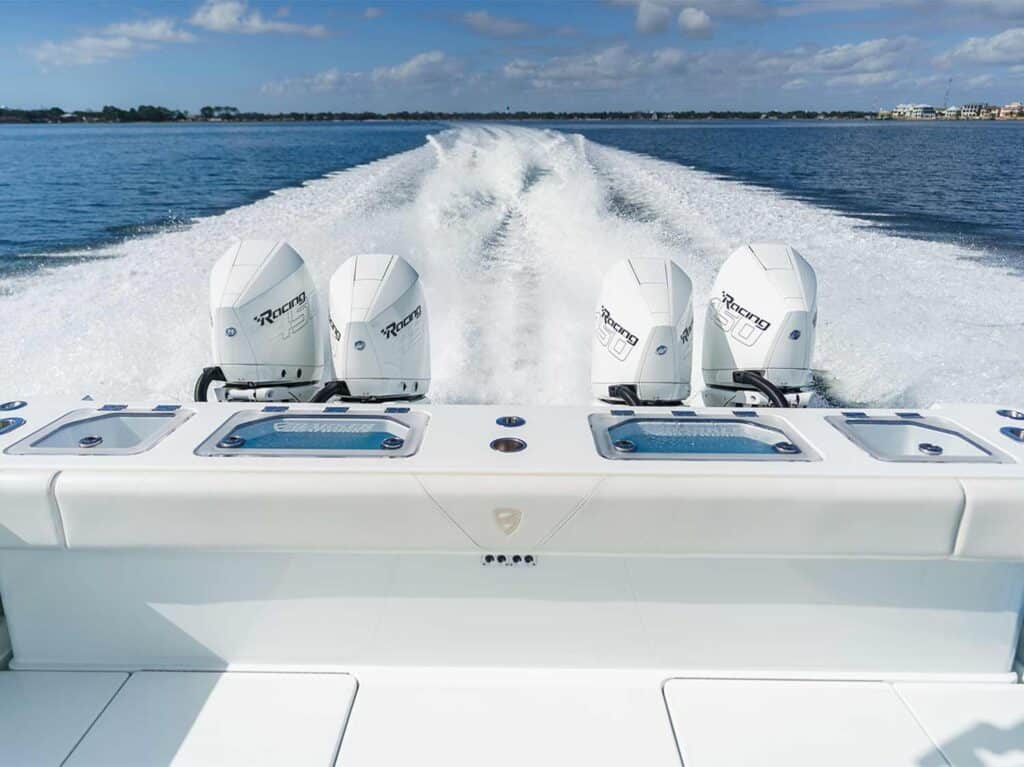 Four outboard boat engines on a sportfishing boat. The wake of the boat can be seen on the water in its trail.