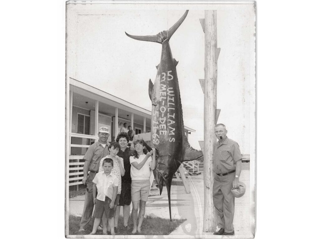 A black and white photo of a family standing next to a large marlin hanging on a boat dock pole.
