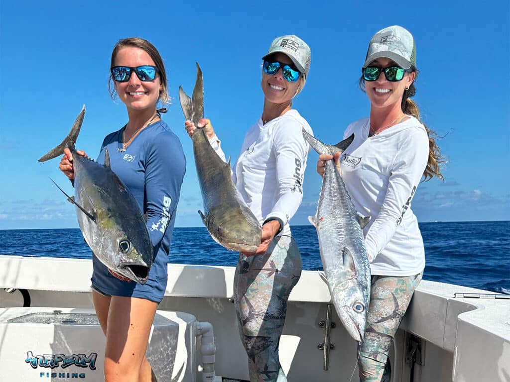 Three women pose and hold up fish that they've caught.