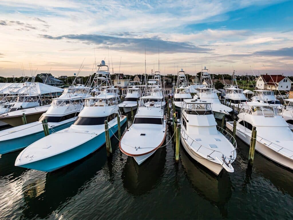 A collection of sport-fishing boats at various sizes/makes docked in the marina at dusk.