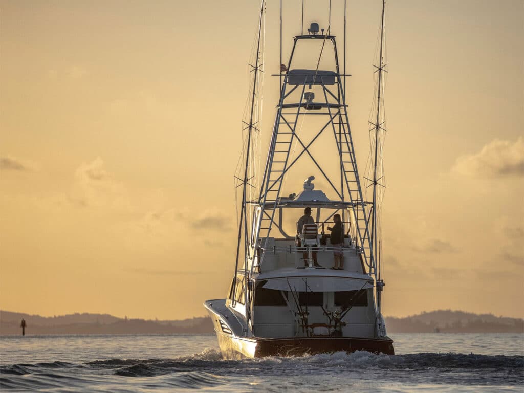 A sport-fishing boat cruises across the ocean at sunset.