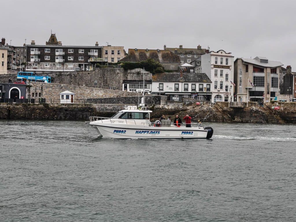 A small outboard boat cruises across the waters along the coastline of Plymouth seaside port.