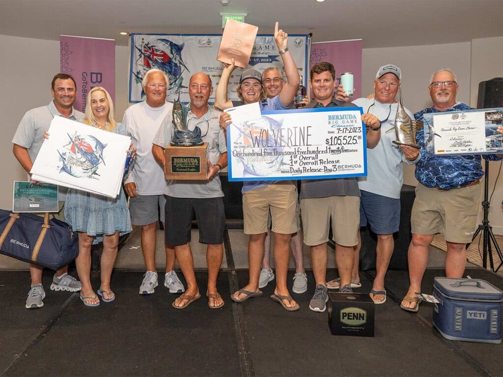 Team Wolverine standing at an awards ceremony holding a large prize check and several prize awards including plaques, tote bags, and trophies.