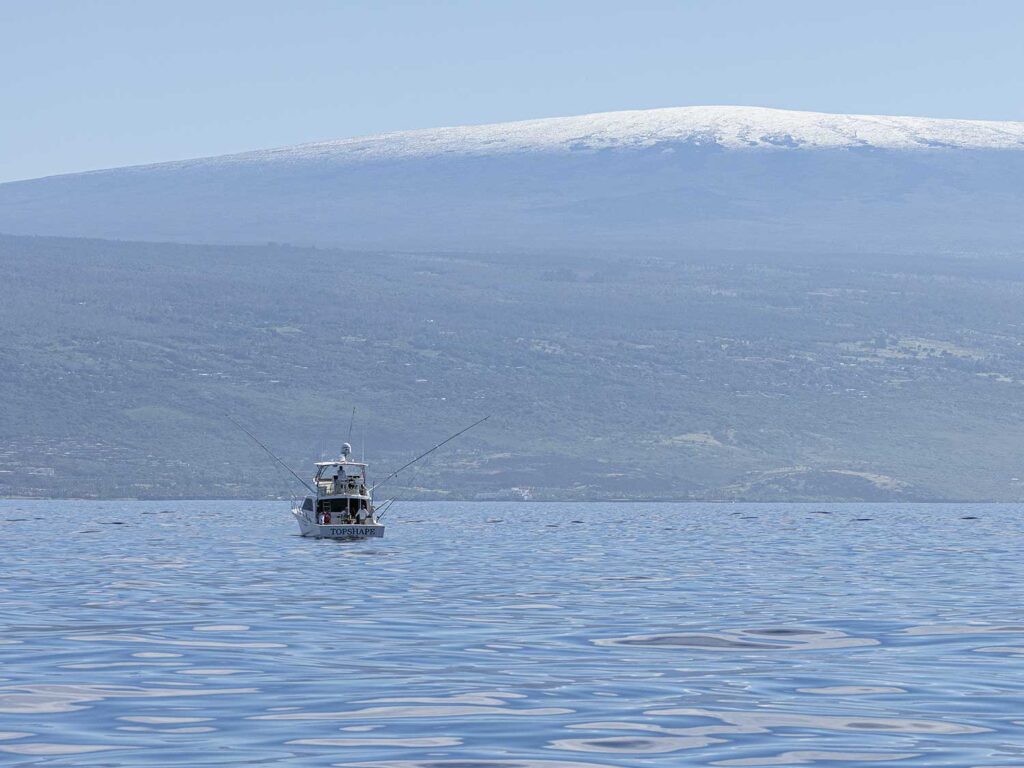 The large mountainous islands of Hawaii seen in the horizon as a sport-fishing boat cruises across the ocean.