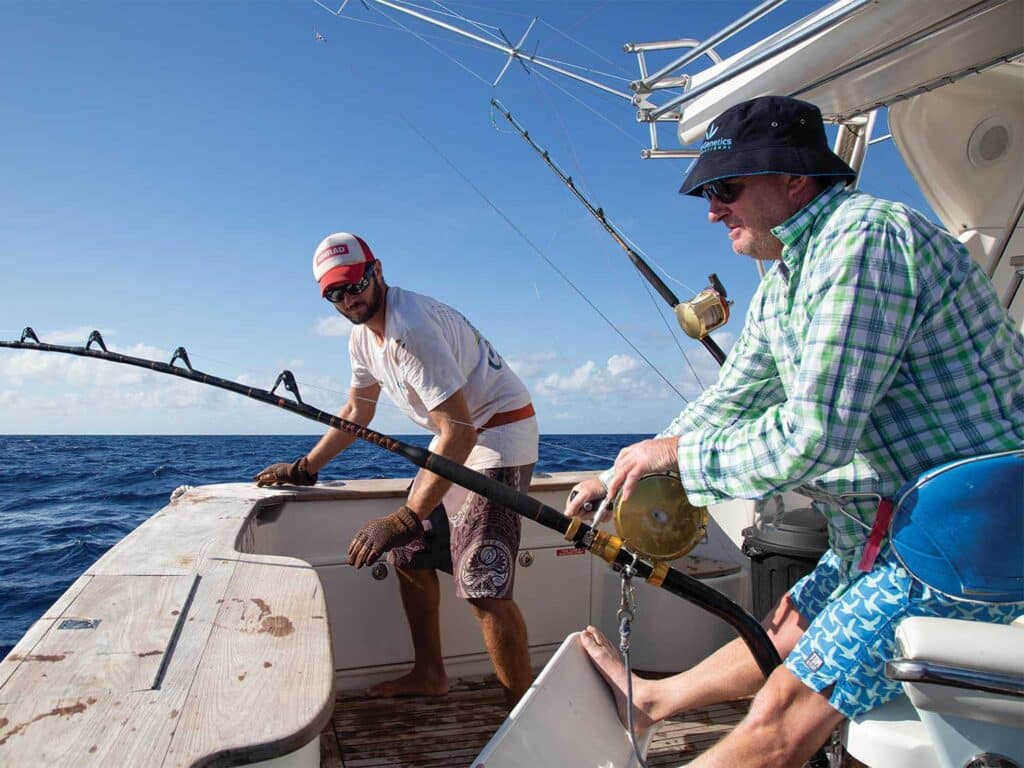 A crewmate watches as a sport-fishing seated in the fighting chair reels in a large marlin.