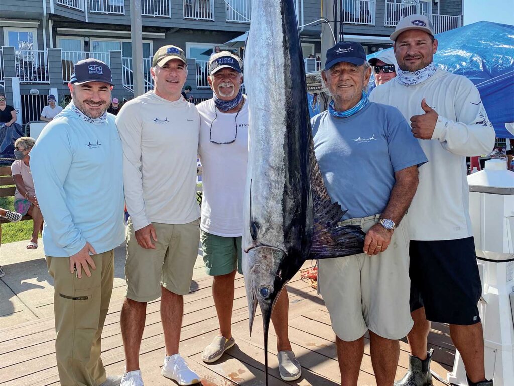A sport-fishing team stands beside a large marlin at a weigh-in station.