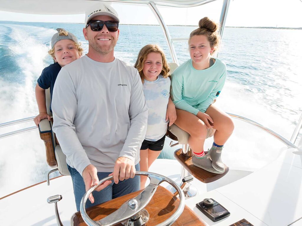 Tim Winters standing at the helm of a sport-fishing boat surrounded by his three children: one son and two daughters.