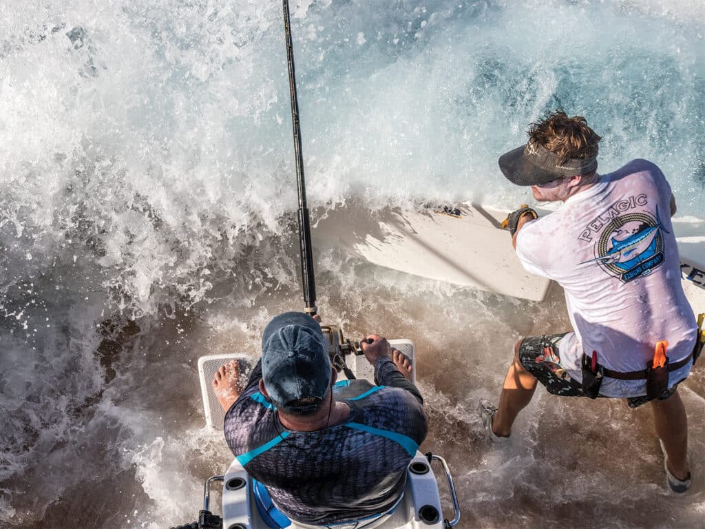 Two anglers fish with heavy tackle while ocean water sprays over the sport-fishing boat's transom.
