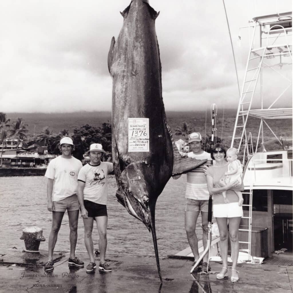 A black and white image of four people standing next to a large record blue marlin.