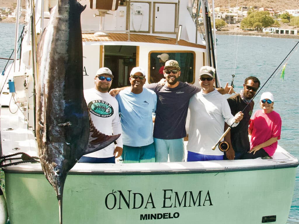 A sport-fishing team stands in the cockpit of a sport-fishing boat next to a large record marlin.