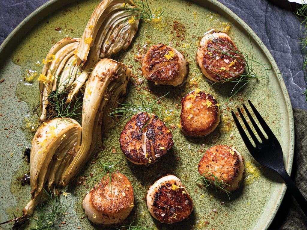 A plate of pan-seared scallops next to seared fennel.
